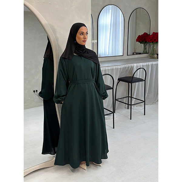 A Women wearing a Emerald Green Satin Silk Type Fabric, called Premium Korean Nida with Zip Pockets, Elasticated Sleeves and Belt with a modal Hijab in Size 52 which fits a size 6-16