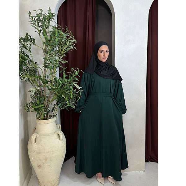 A Women wearing a Emerald Green Satin Silk Type Fabric, called Premium Korean Nida with Zip Pockets, Elasticated Sleeves and Belt with a modal Hijab in Size 52 which fits a size 6-16