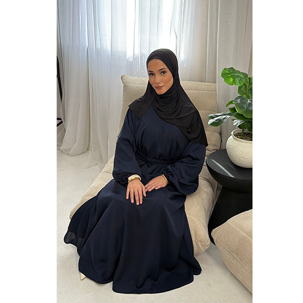 A Women wearing a Navy Satin Silk Type Fabric, called Premium Korean Nida with Zip Pockets, Elasticated Sleeves and Belt with a modal Hijab in Size 52 which fits a size 6-16
