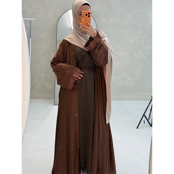 A Women Wearing A Brown Floral Embroidered Elegant Detailed Sleeve Open Button A-Line Cut  Abaya In Shiny Satin Type Fabric with Side Pockets in Size 52 fits a Size 6-16