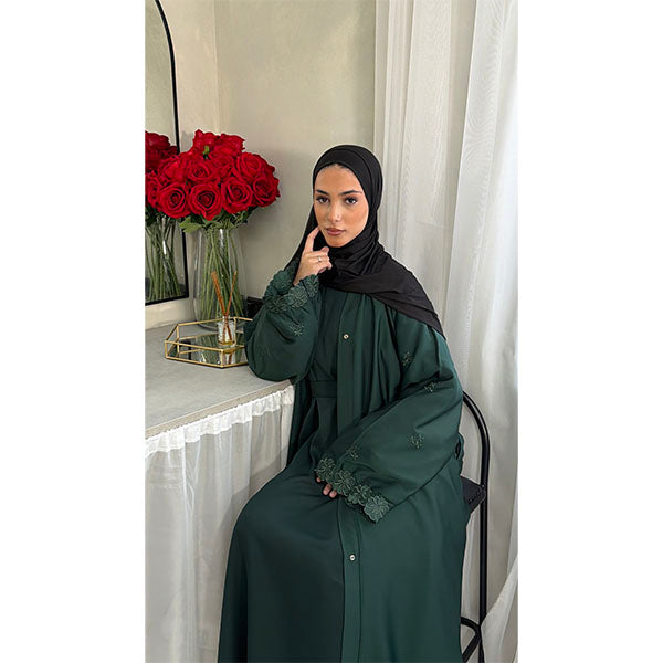 A Women Wearing A Emerald Green Floral Embroidered Elegant Detailed Sleeve Open Button A-Line Cut  Abaya In Shiny Satin Type Fabric with Side Pockets in Size 52 fits a Size 6-16