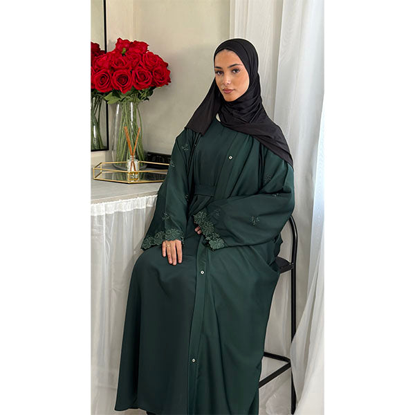 A Women Wearing A Emerald Green Floral Embroidered Elegant Detailed Sleeve Open Button A-Line Cut  Abaya In Shiny Satin Type Fabric with Side Pockets in Size 52 fits a Size 6-16
