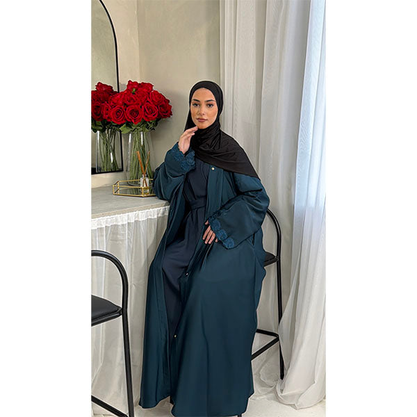 A Women Wearing A Teal  Floral Embroidered Elegant Detailed Sleeve Open Button A-Line Cut  Abaya In Shiny Satin Type Fabric with Side Pockets in Size 52 fits a Size 6-16