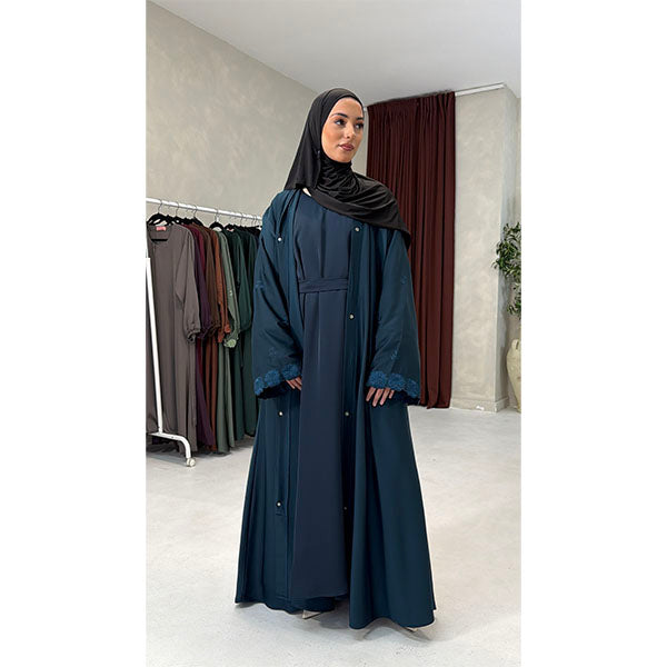 A Women Wearing A Teal  Floral Embroidered Elegant Detailed Sleeve Open Button A-Line Cut  Abaya In Shiny Satin Type Fabric with Side Pockets in Size 52 fits a Size 6-16