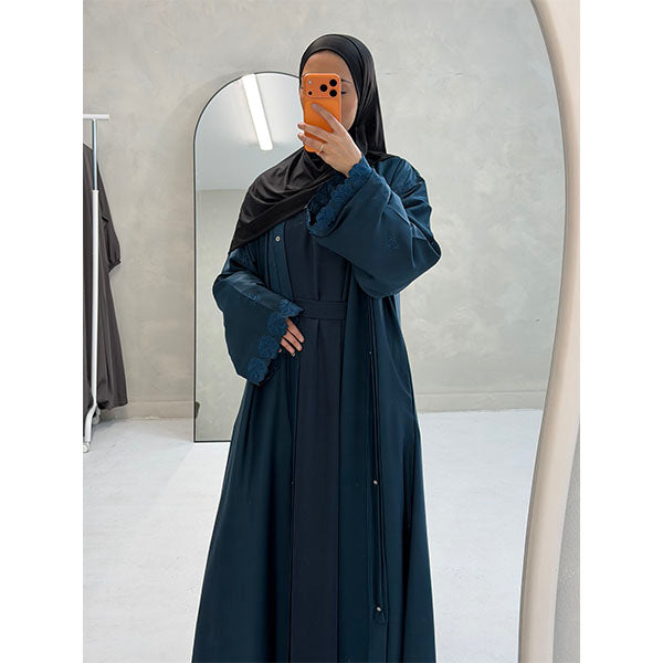 A Women Wearing A Teal  Floral Embroidered Elegant Detailed Sleeve Open Button A-Line Cut  Abaya In Shiny Satin Type Fabric with Side Pockets in Size 52 fits a Size 6-16